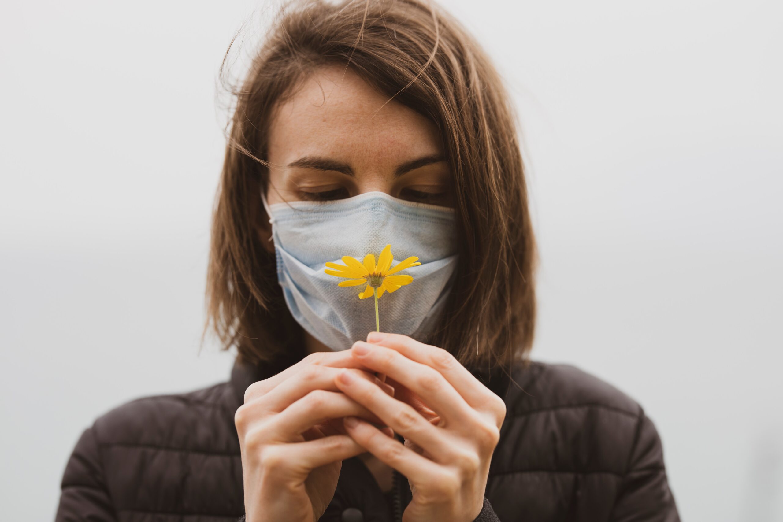 Donna che tiene tra le mani un fiore, ma indossa una mascherina come a proteggersi dal polline